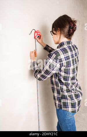 Woman worker measuring and marking distance on white wall with measure tape tool and pencil Stock Photo