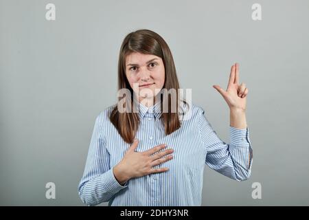 Handsome with hand on chest and fingers up, making a loyalty promise oath. Young beautiful standing over isolated background smiling swearing arm on thorax fingers up. Young attractive woman Stock Photo