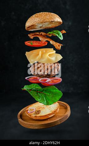 Flying hamburger with ingredients on dark stone background. Creative still life concept Stock Photo