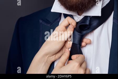 Womens hands tie around the neck of men classic suit model beard Stock Photo