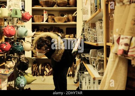 Masked shopper in a winter jacket examines teapots in s small kitchen store in Ottawa, Ontario, Canada. Stock Photo