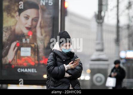 Kiev, Ukraine. 12th Dec, 2020. A woman wearing a face mask as a preventive measure against the spread of COVID-19 coronavirus uses her a mobile phone while standing next to Chanel perfume advertising in downtown Kiev. Credit: Pavlo Gonchar/SOPA Images/ZUMA Wire/Alamy Live News Stock Photo