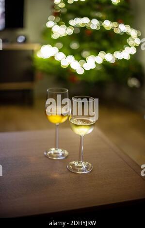 Two glasses of wine indoors at home in front of Christmas tree and lights on the wooden table Stock Photo