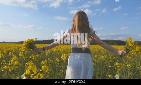 A girl in a white dress runs among a rapeseed field. Stock Photo