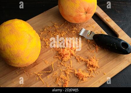 Zesting Navel Oranges: Two oranges and a zester on a bamboo cutting board Stock Photo