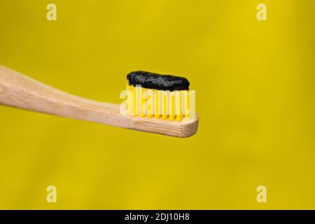 Eco friendly natural bamboo toothbrush with black charcoal whitening toothpaste isolated on yellow background Stock Photo