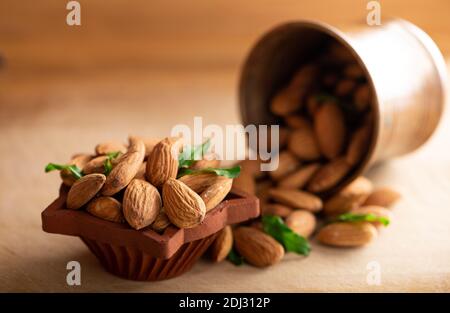 Group of almond nuts with leaves in clay bowl with background of almond in copper bowl from sacking on a wooden table. Stock Photo