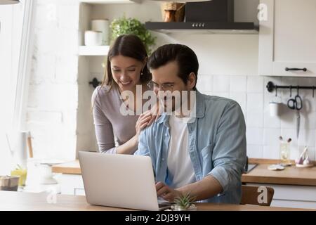 Happy young couple using laptop in modern kitchen together Stock Photo