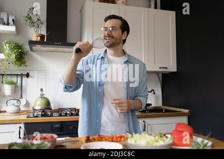 Smiling funny young man wearing glasses singing into whisk Stock Photo