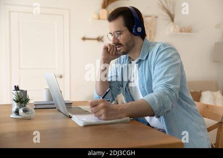 Serious man wearing glasses using laptop, writing notes, working online Stock Photo
