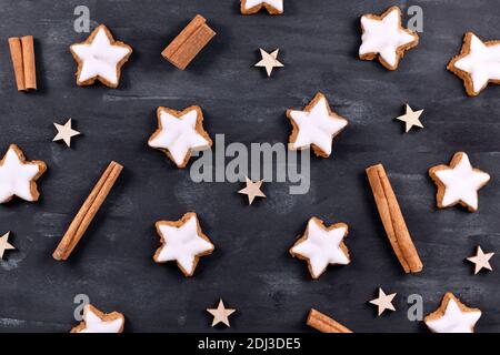Traditional German star shaped glazed cinnamon Christmas cookies called 'Zimtsterne' on dark black background with star ornaments and cinnamon sticks Stock Photo