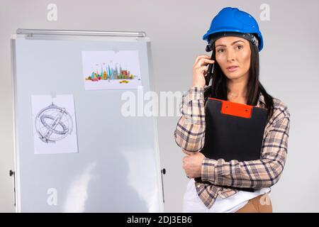 Woman architect in hardhat, talking on the phone and holds a black folder with documents in her hands. Gender equality. Stock Photo