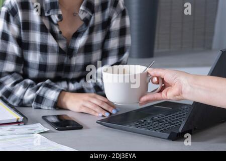 close up of a young woman working from home and her mother gives her a cup of coffee. Stock Photo