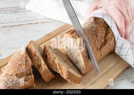 Woman hand cutting loaf of bread on white wooden table. Loaf of wholegrain bread Stock Photo
