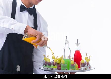 Closeup of a waiter holding a tray and mixing liquor in glass shots with grapes on a light background. Service and vegan cocktails concept. Stock Photo