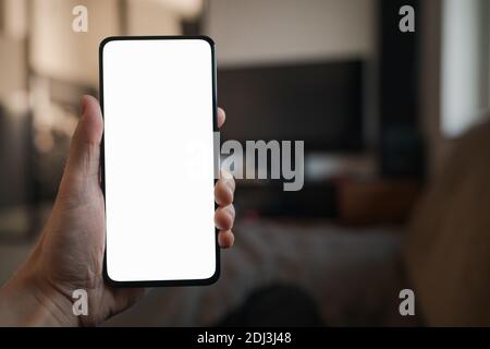 POV photo of man holding smartphone with white screen while sitting on a couch, shallow focus Stock Photo