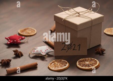Christmas gift box from eco friendly paper wrapped with natural twine on wood table with natural decorations and 2021 card, shallow focus
