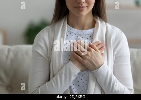 Close up wishful peaceful young woman holding hands on chest