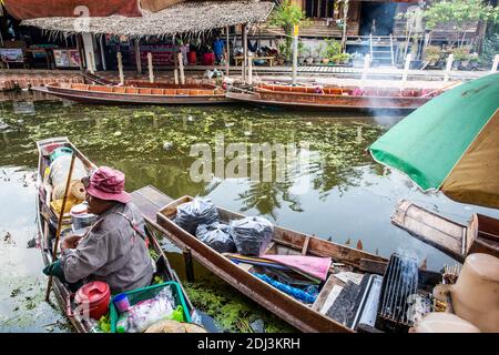 Women aboard san pans cook and serve a variety of snack and entree street food dishes in the Damnoen floating market near Bangkok. Stock Photo