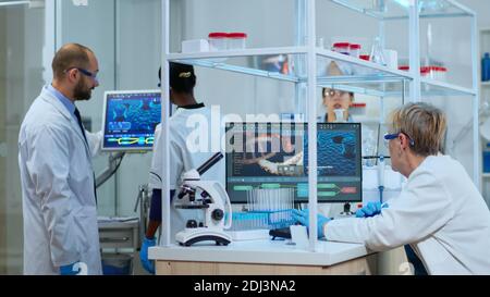 Multiethnic team working to develop a new vaccine in modern equipped laboratory. Diverse group of biochemistry scientists examining virus evolution using high tech for researching treatment Stock Photo