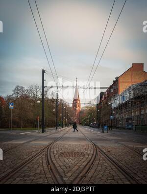 Lund, Sweden - November 29, 2020: A woman crosses the cobblestoned street in front of church Allhelgonakyrkan Stock Photo