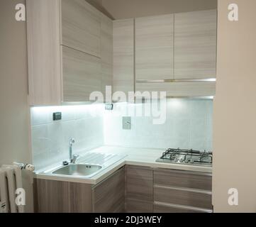 View of a modular corner kitchen in gray and brown color, the led under-cabinet light attracts attention. Stock Photo