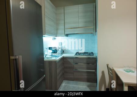 View of a modular corner kitchen in gray and brown color, the led under-cabinet light attracts attention. Stock Photo