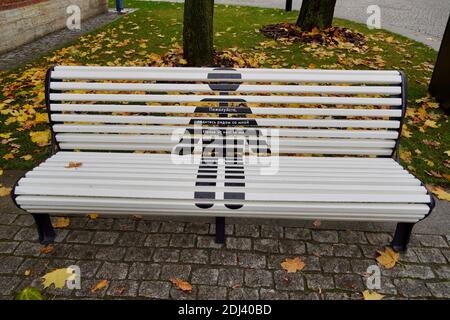 Empty grey bench in the park against the background of autumn leaves Sign Please sit next to me, Pandemic time, Amazing man is drawing on the bench