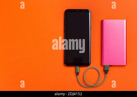 Smartphone Charging with Power Bank on Orange Background. Space for text. Top View. Stock Photo