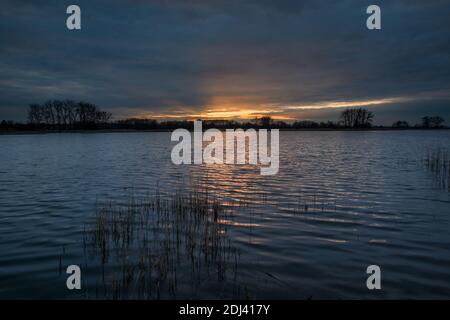 Sunset over a quiet lake and dark clouds in the evening, spring view Stock Photo