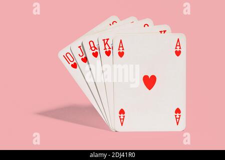 Winning hand of playing cards in poker showing a royal flush or straight flush in the suit of hearts ace through ten on pink background with shadow Stock Photo