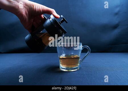 French press and herbal tea, on black background among dry leaves