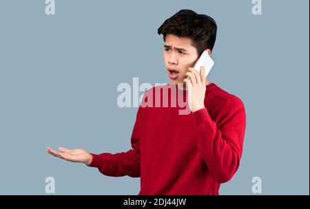 Confused asian man talking on smartphone at studio Stock Photo