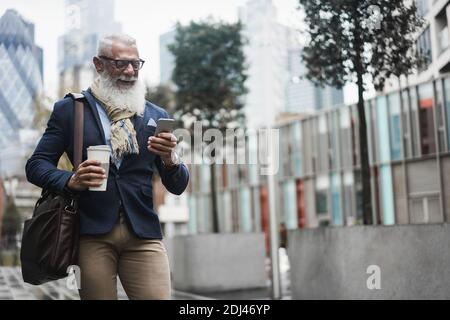 Hipster senior business man using mobile phone and drinks coffee while going to work - Focus on face Stock Photo