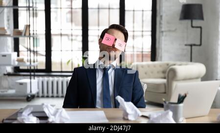 Tired sleepy businessman with stickers on eyes sleeping at workplace Stock Photo