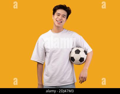 Asian man posing with soccer ball on orange background Stock Photo