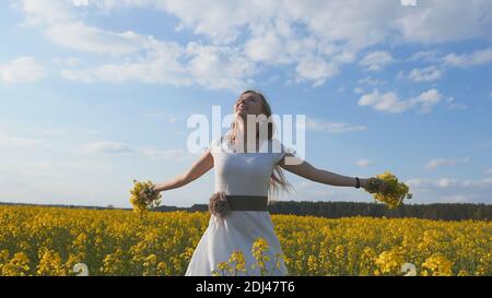 A girl in a white dress is spinning among a rapeseed field. Stock Photo