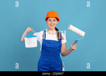 Happy Young Painter Lady Wearing Coveralls Holding Bucket And Equipment For Painting Stock Photo