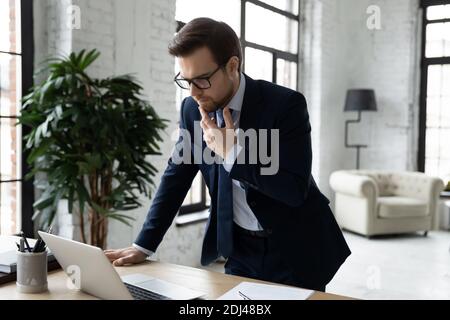 Thoughtful businessman pondering strategy, using laptop, standing near desk Stock Photo