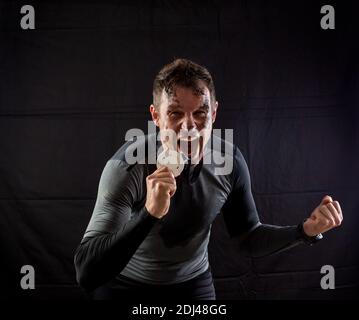 Handsome man in sportswear is insanely rejoicing at the received silver medal in the studio on a black background Stock Photo