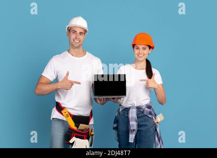 Home Repair Website. Couple In Hard Hats Holding Laptop With Black Screen Stock Photo