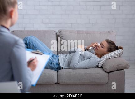 Depressed young woman consulting psychologist, lying on couch and crying Stock Photo