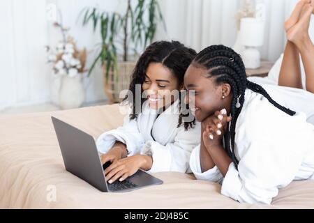 Beautiful black girlfriends reading beauty blog, laying on bed Stock Photo