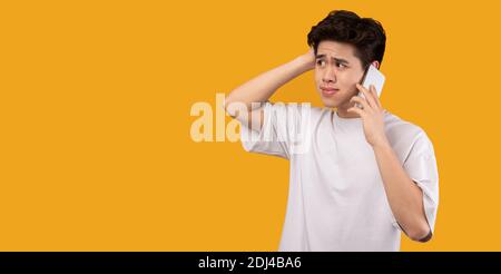 Confused asian man talking on mobile phone at studio Stock Photo