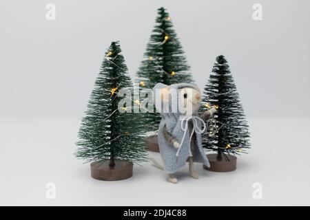 White little rat among beautiful holiday trees in the forest. A toy in the form of a plush rat Stock Photo