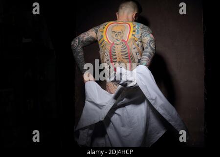 Rare view of young handsome masculin man , in unfastened denim shirt with tattoos all over his back Stock Photo