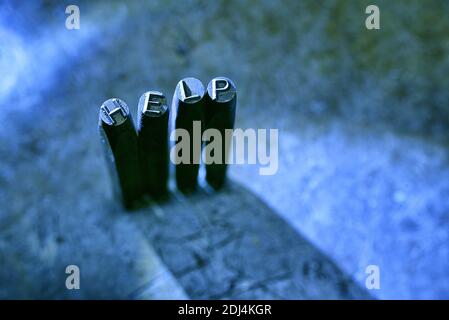 A 'HELP' word composed with metal marking punch on grunge blur background Stock Photo