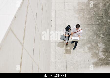 Proud young man showing project he was working on to colleague when they are walking along office building Stock Photo