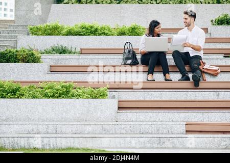 Young smiling managers sitting outdoors, discussing statistics and project details Stock Photo