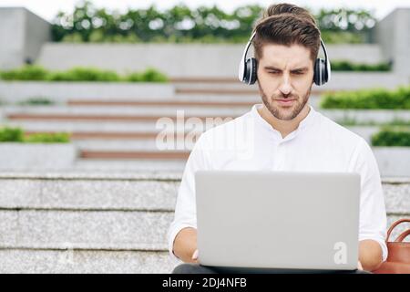 Frowning university student sitting on steps on campus and working on laptop Stock Photo